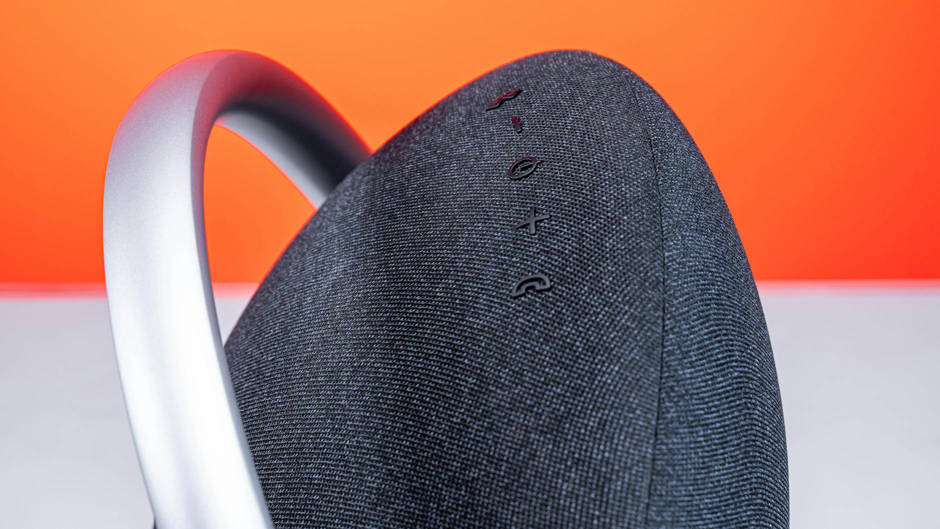 Close-up of a stylish wireless speaker with a handle against an orange background, emphasizing modern design.